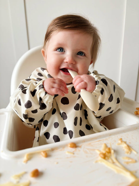 Baby in a high chair with a polka dot bib eating food.
