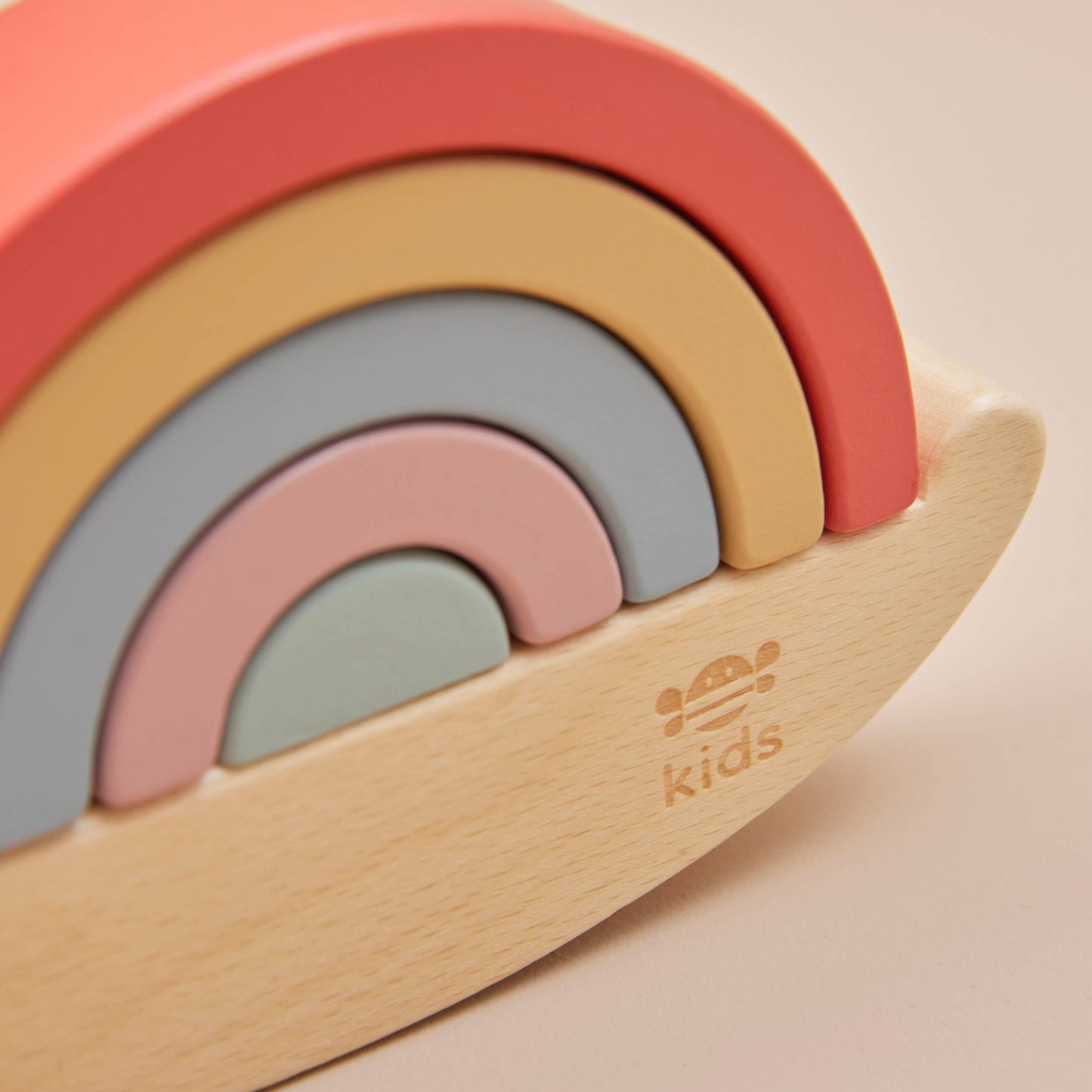Colorful wooden toy with rainbow design on a beige background, featuring the 'kids' brand logo.