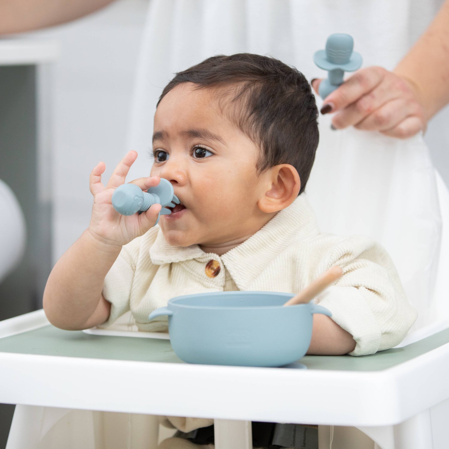 Baby feeding themselves with spoon from bowl