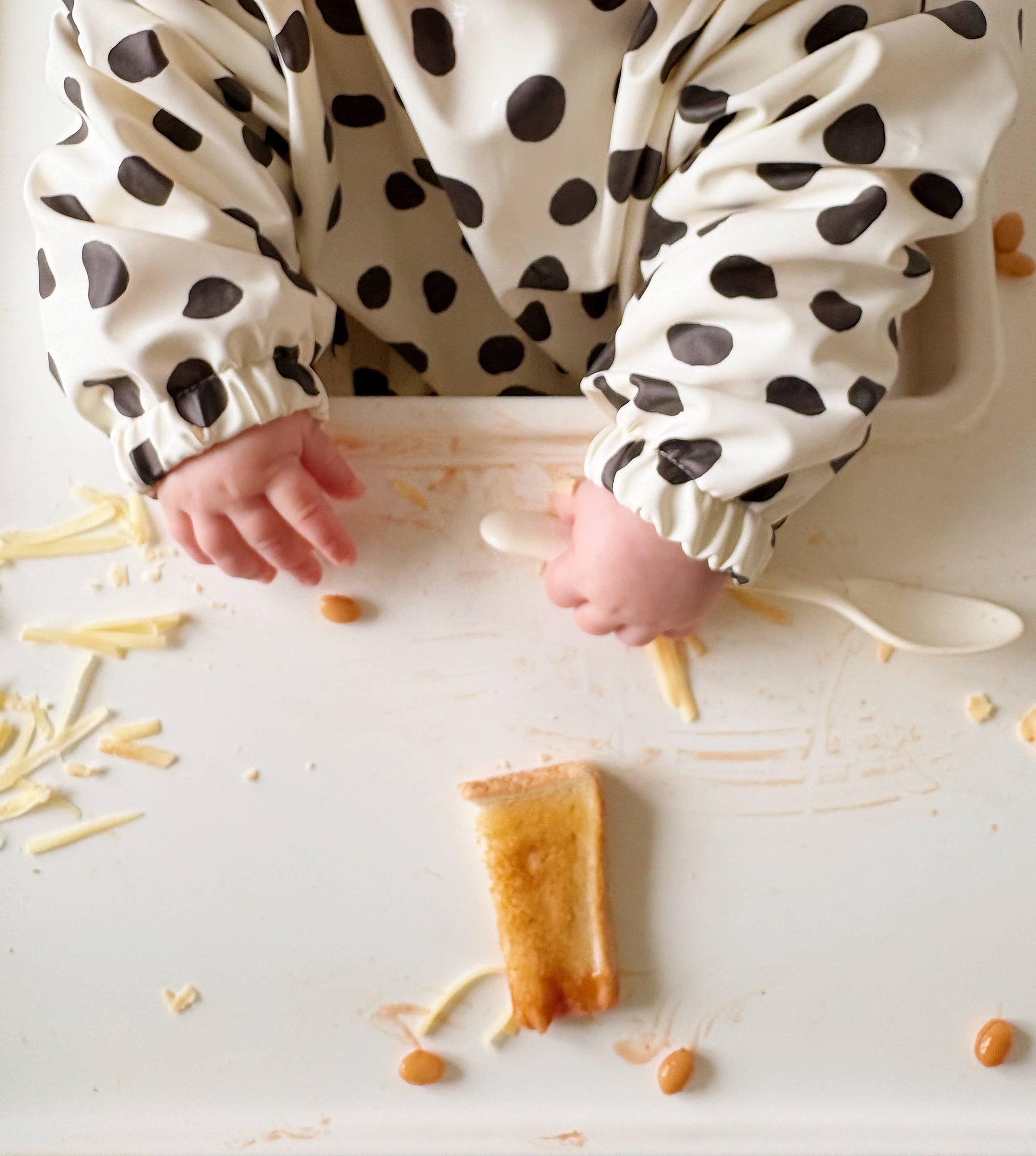 Child's hands reaching for food on a white surface with a polka dot bib.