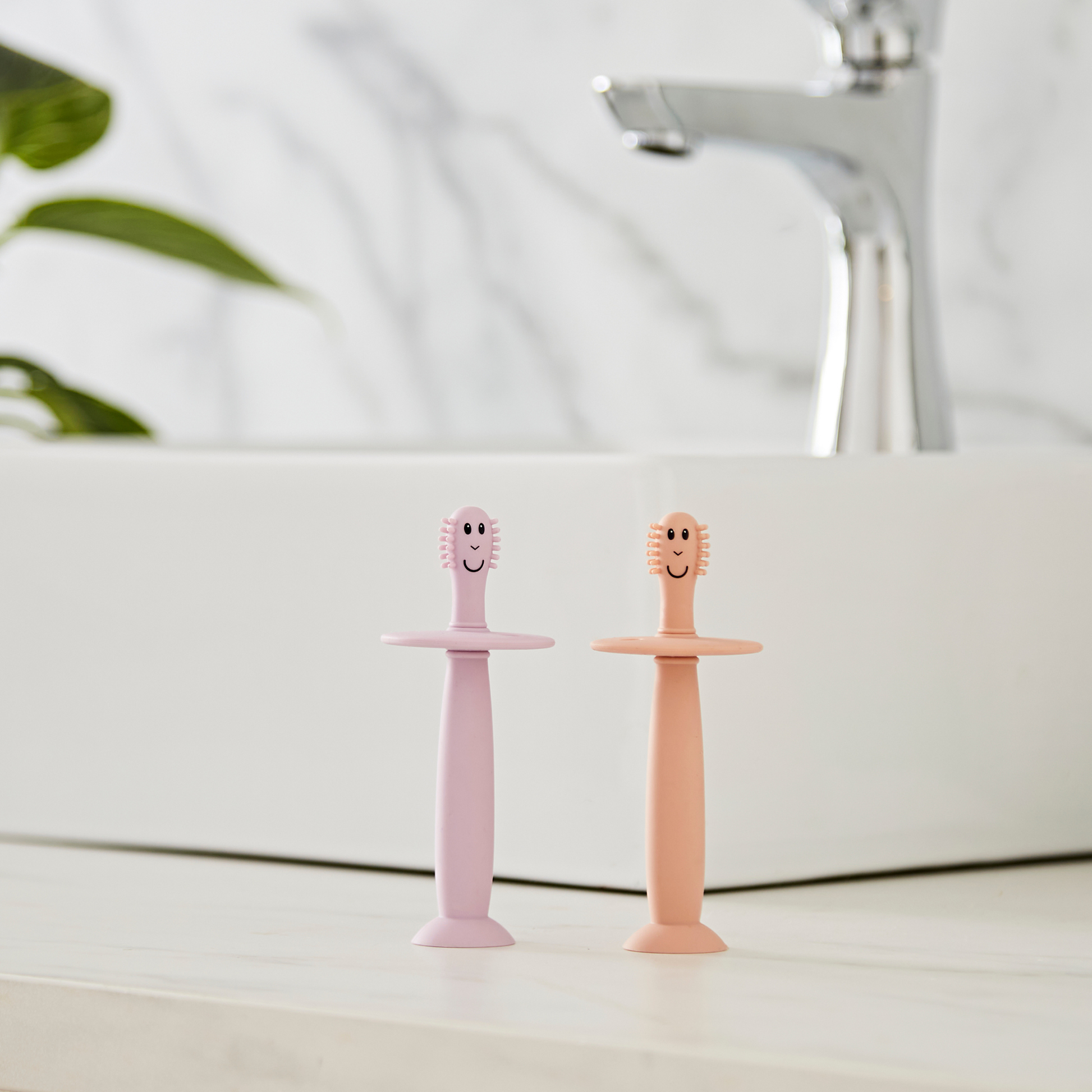 Two children's toothbrushes with smiling faces on a bathroom counter.