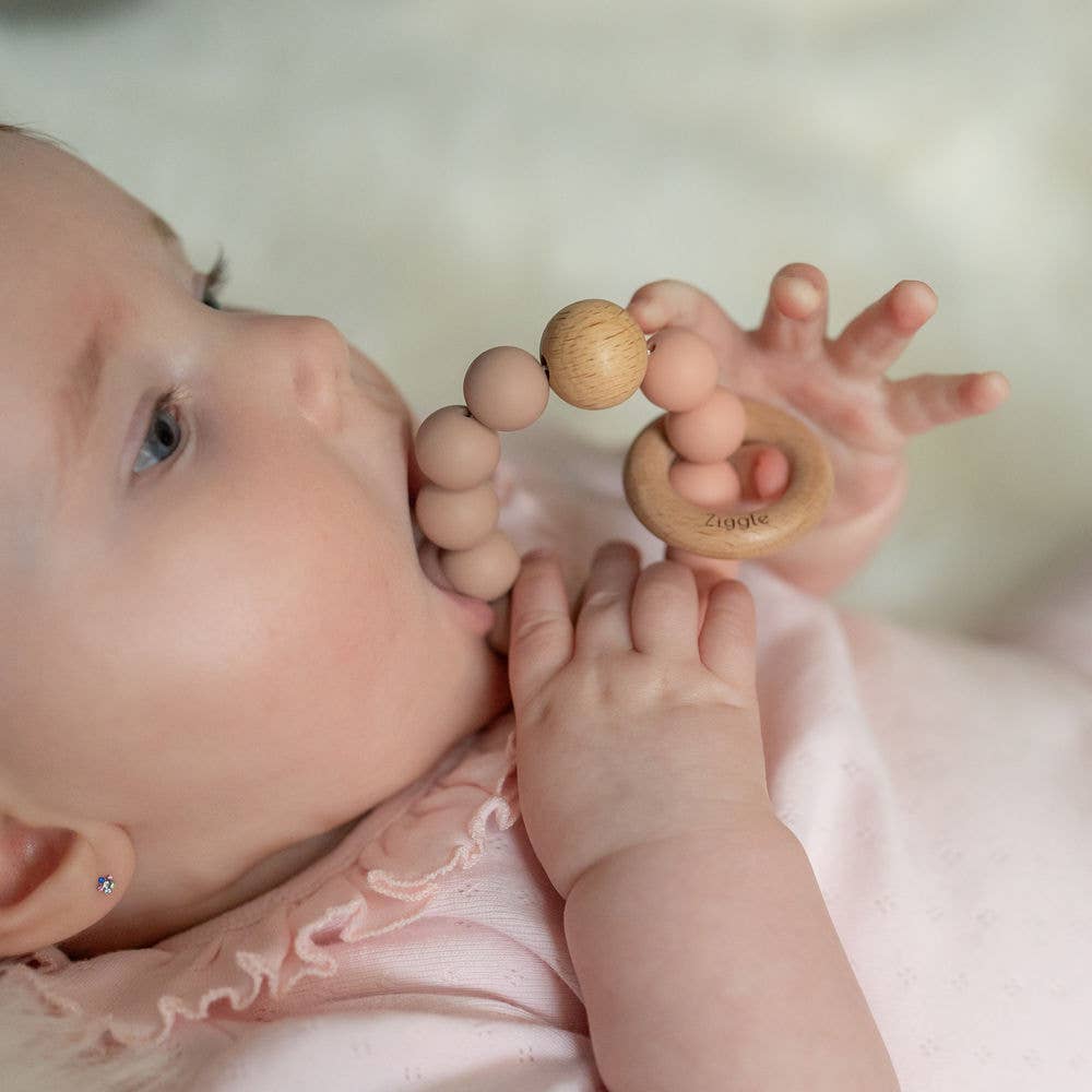 Baby holding a wooden teething ring with 'Lolly' engraved on it.