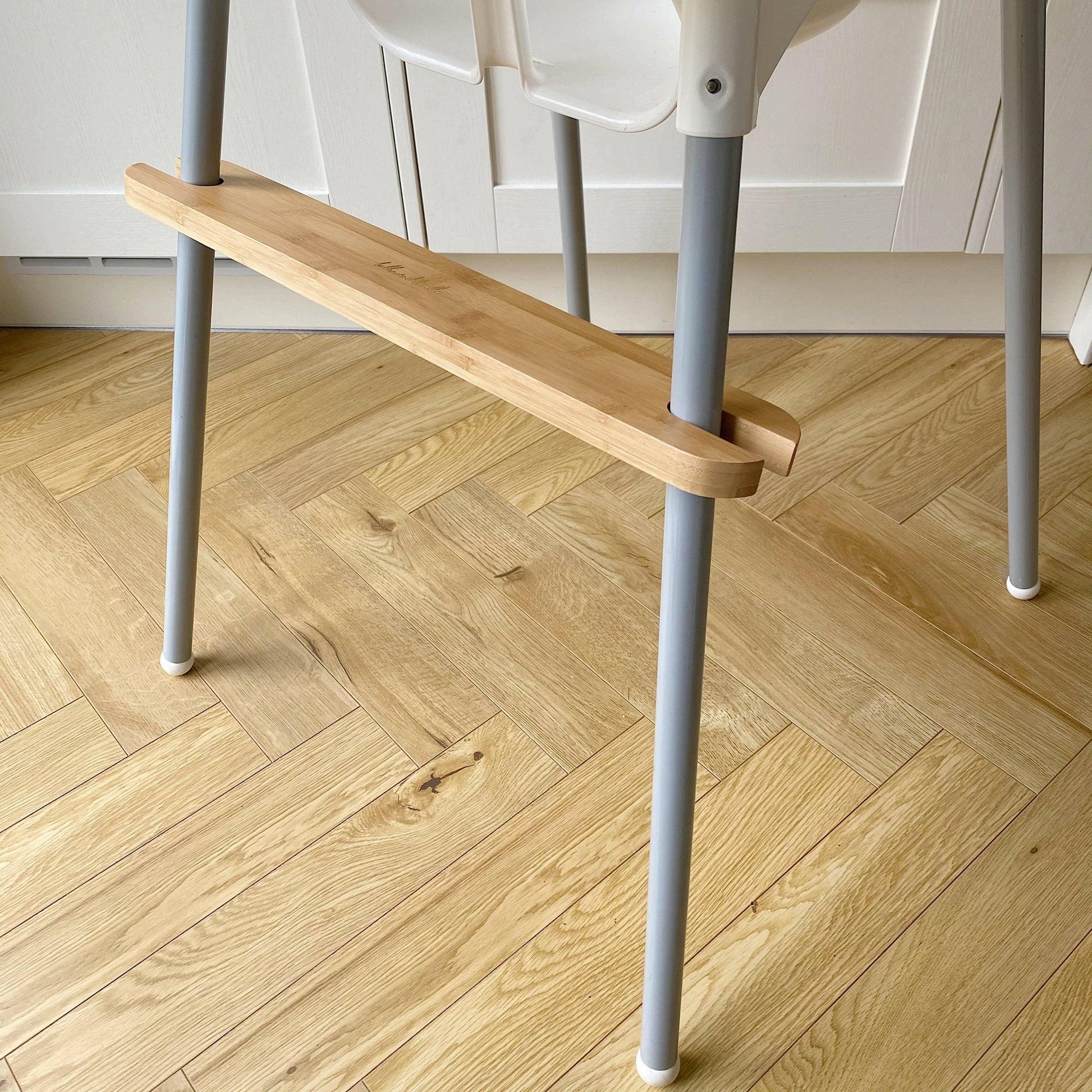 Wooden footrest with grey metal highchair legs on a wooden floor