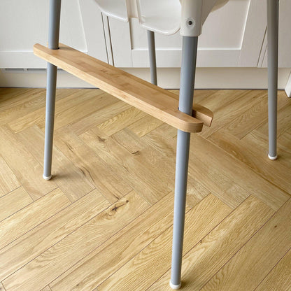 Wooden footrest with grey metal highchair legs on a wooden floor