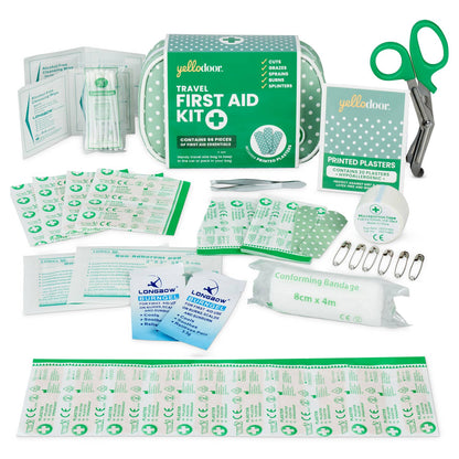 Travel first aid kit with various supplies including bandages, plasters, and scissors on a white background.