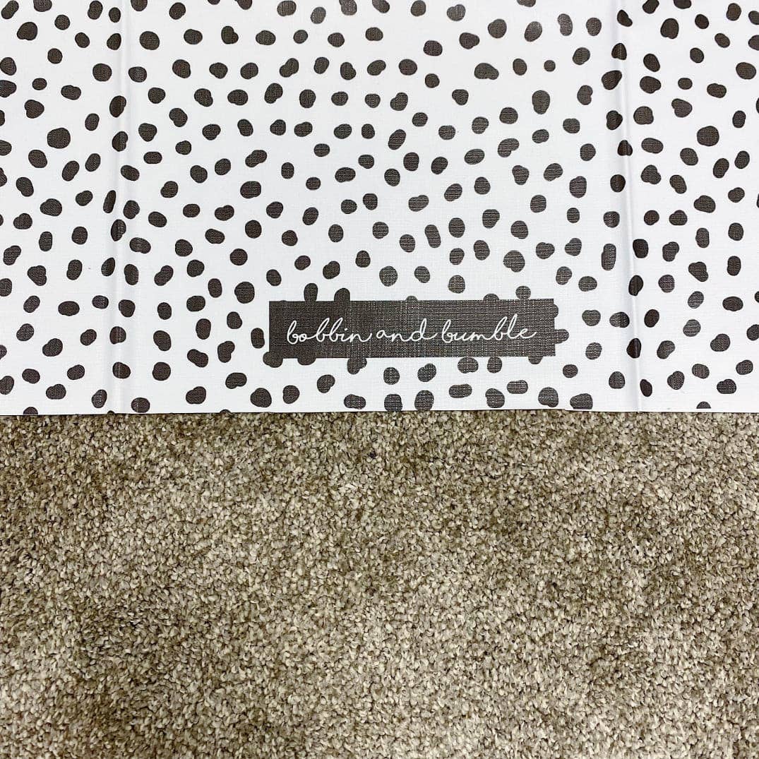 Patterned splashmat with black dots on a white background and a visible brand label.