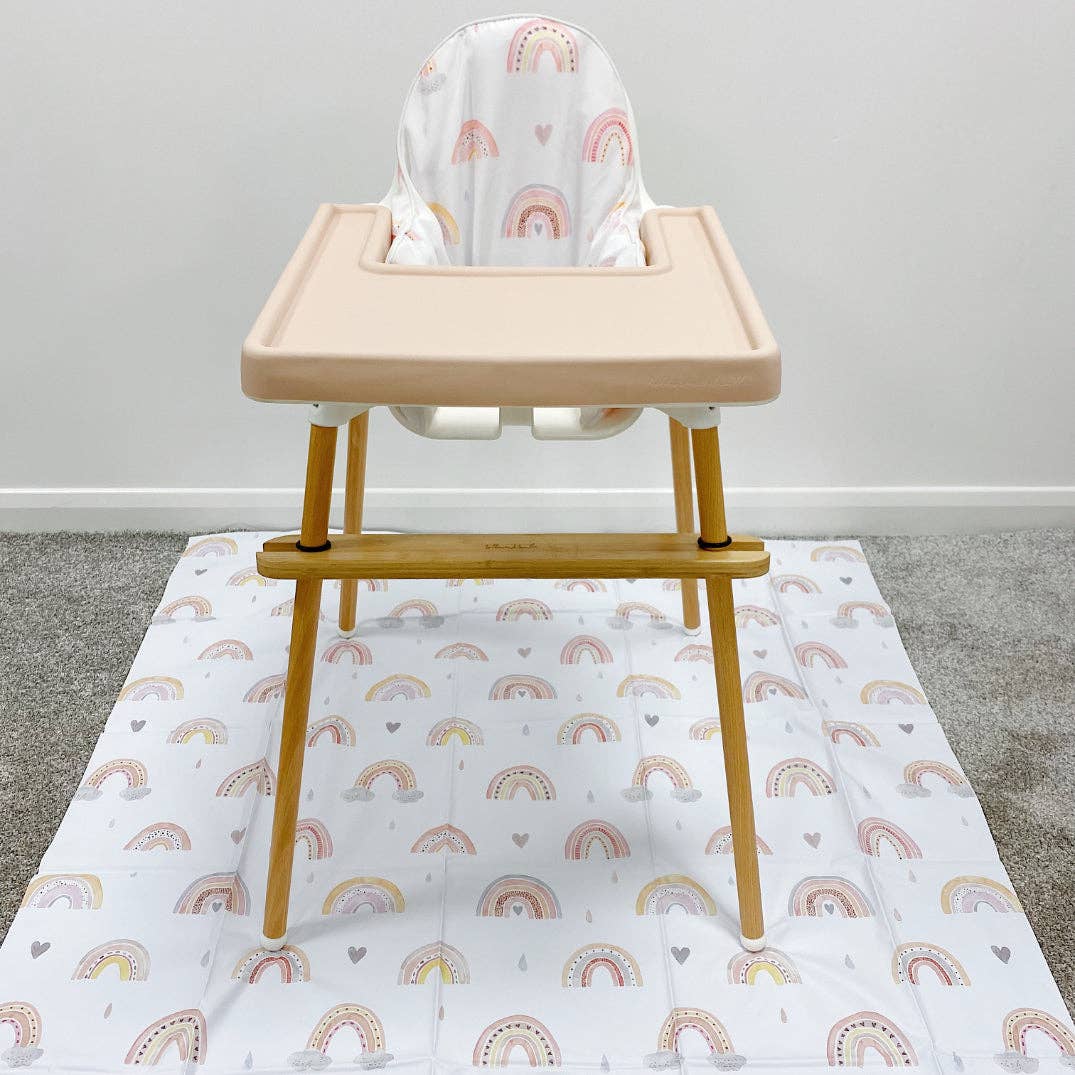 Wooden high chair with a white cover on a splashmat with rainbow pattern