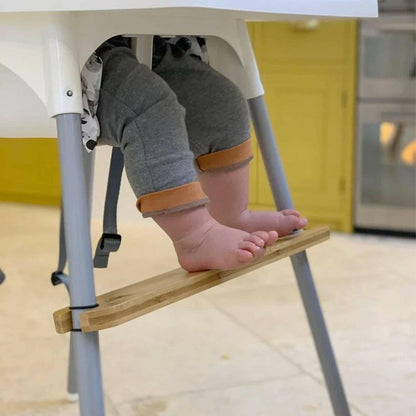Child's legs and feet on a high chair with a wooden footrest in a kitchen setting.