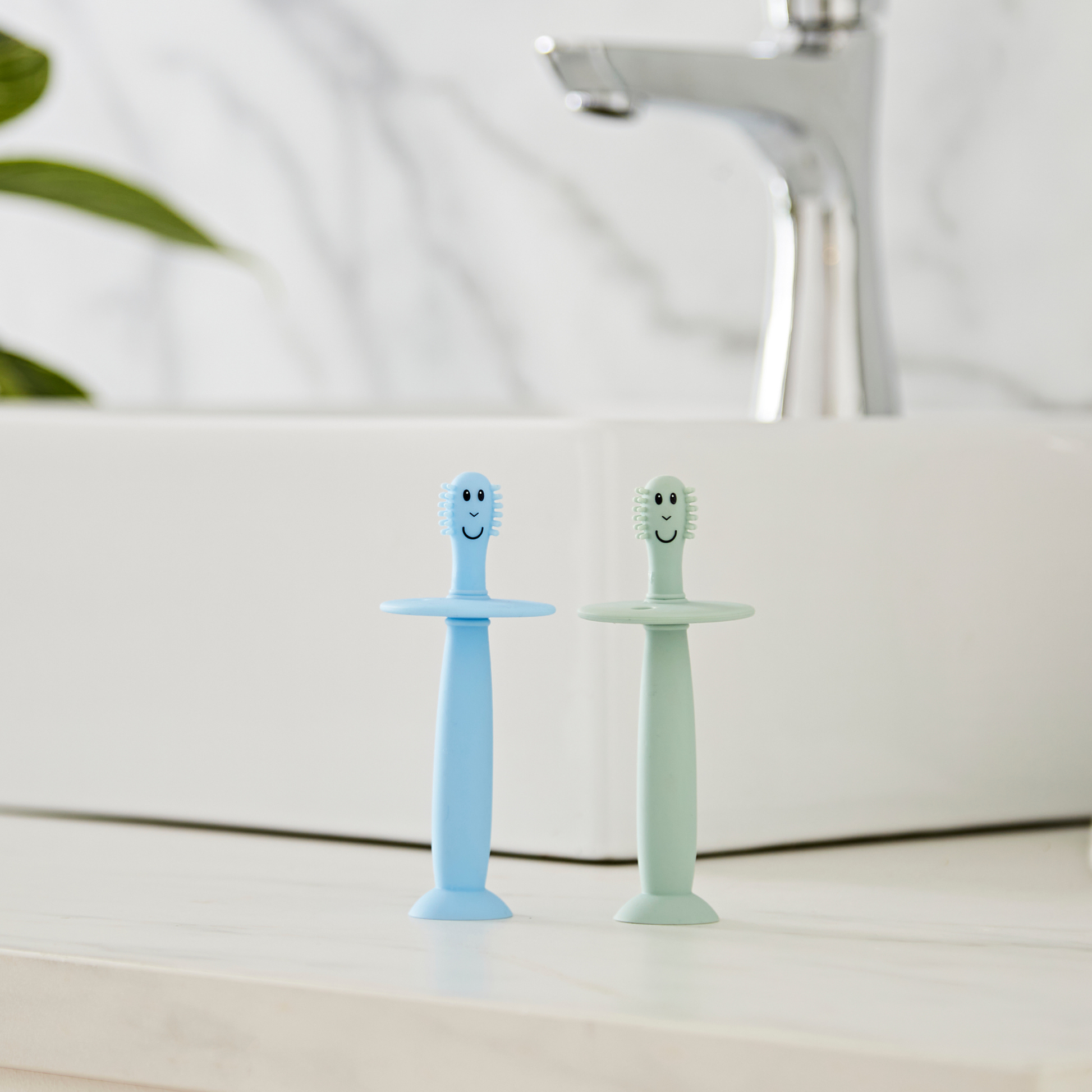 Two cartoon-style toothbrushes, one blue and one green, on a bathroom counter.