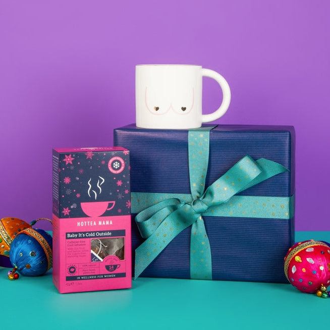 White mug on a blue gift box with a pink box and decorative items on a purple and teal background