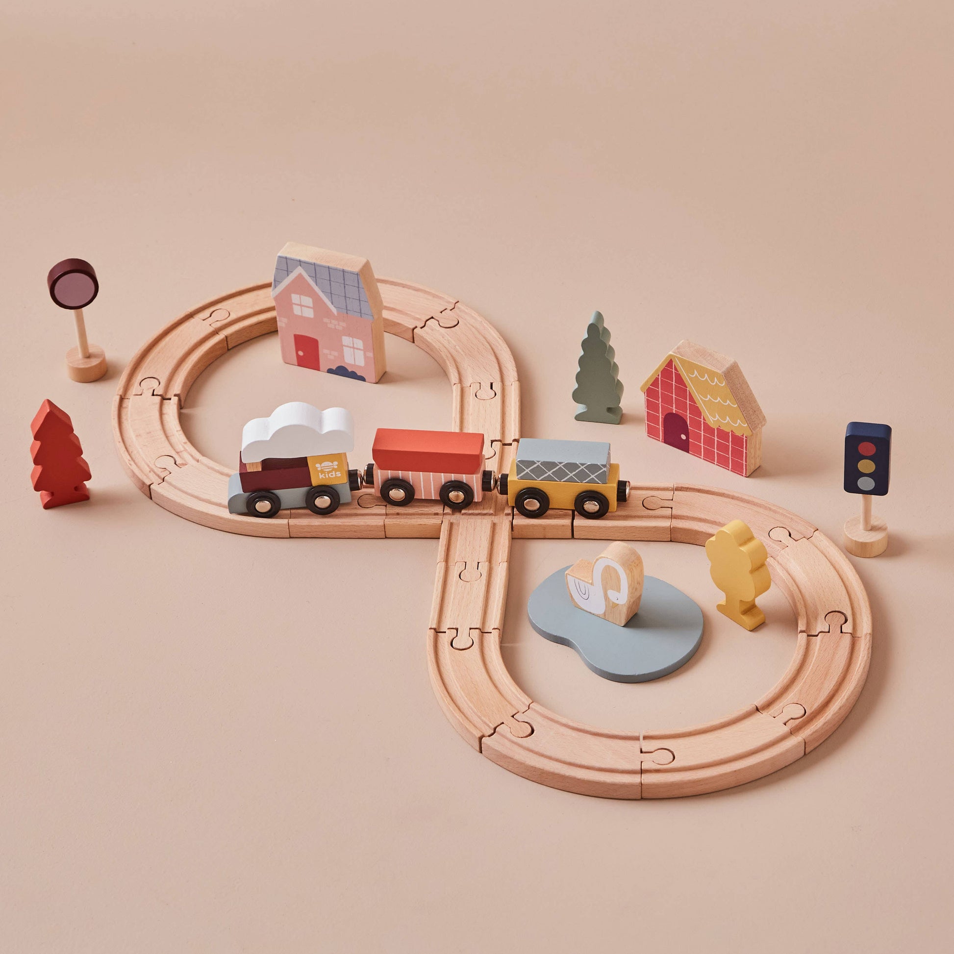 Wooden train set with tracks, cars, and small buildings on a beige background
