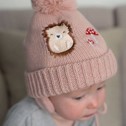 Child wearing a pink knit hat with a lion design and red mushroom on a blurred background