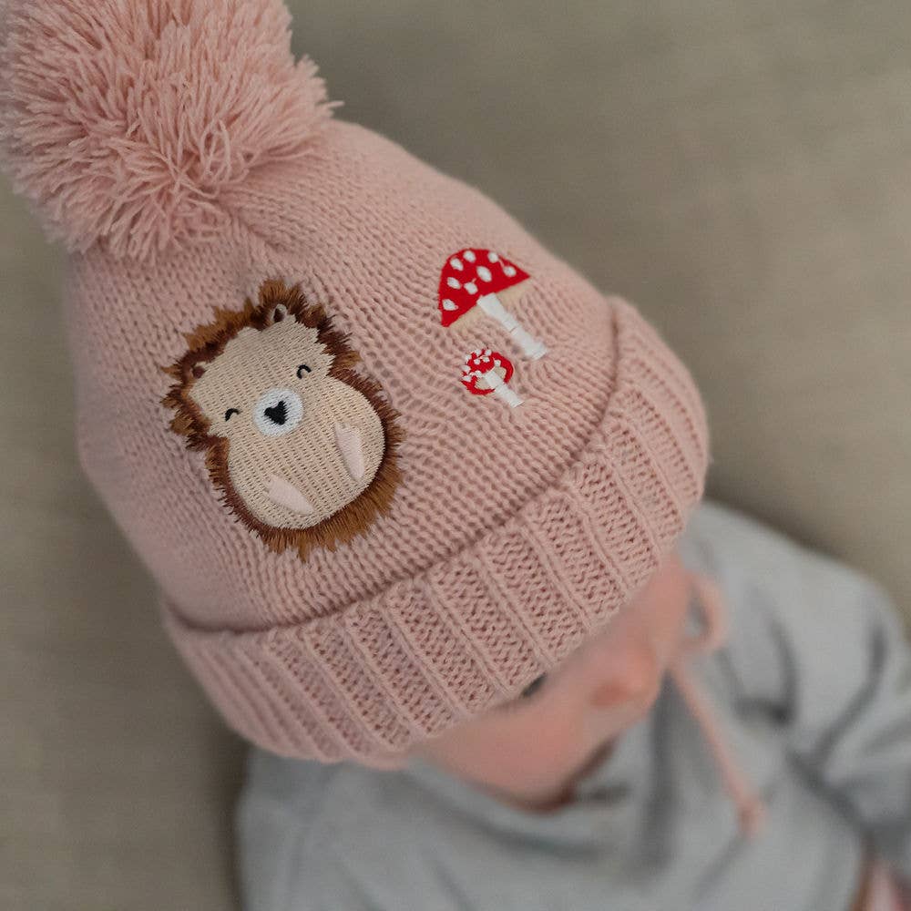 Pink knitted hat with a hedgehog and mushroom design on a neutral background