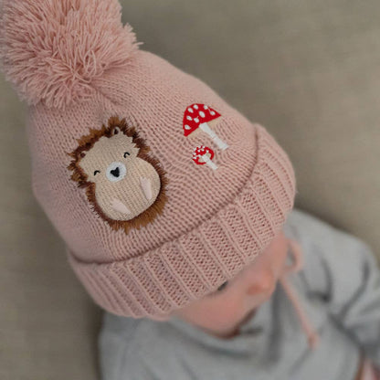 Pink knitted hat with a hedgehog and mushroom design on a neutral background