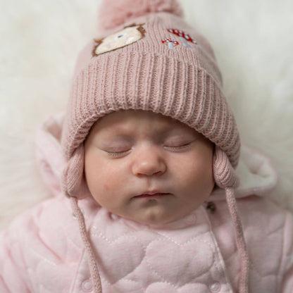 Baby wearing a pink knitted hat with ears and a matching outfit on a light background