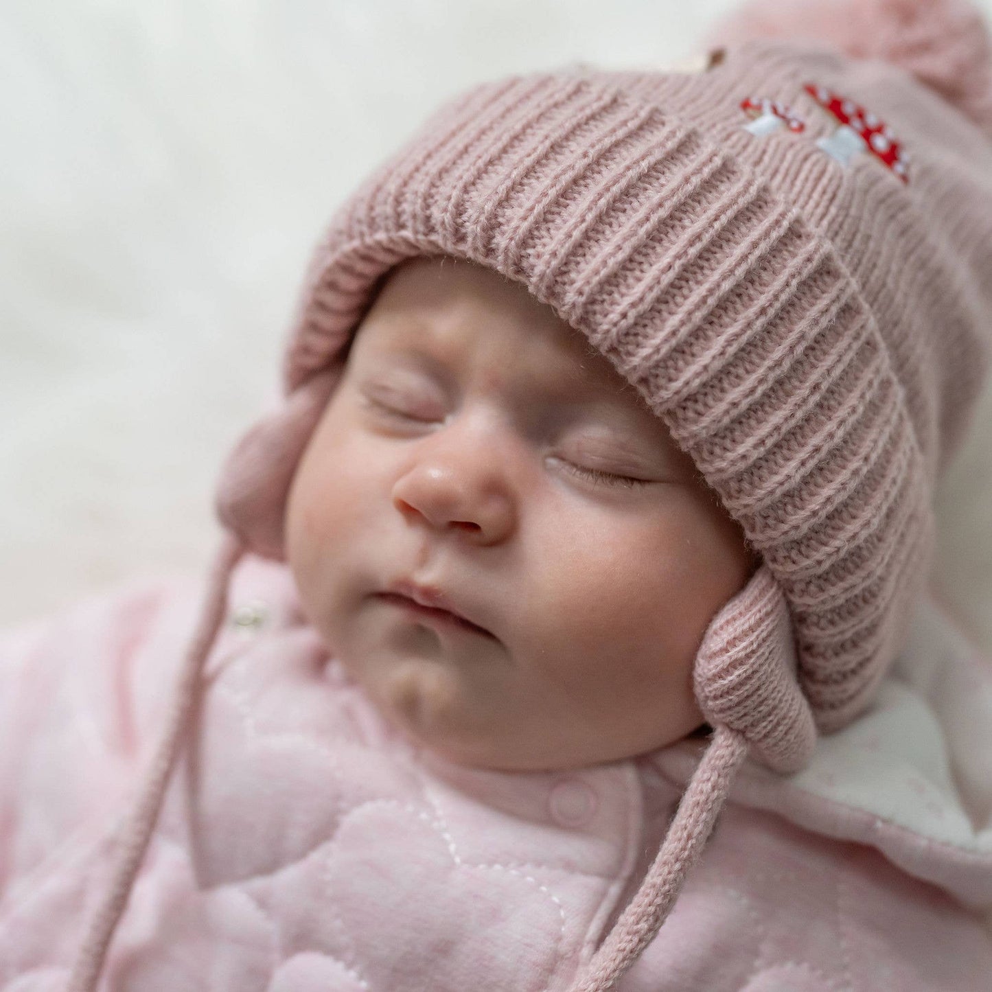 Newborn baby wearing a pink knitted hat and coat on a soft background