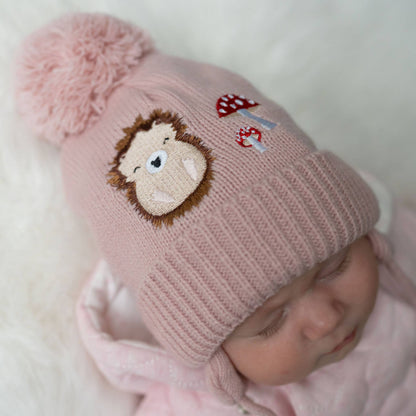 Pink knitted baby hat with a monkey face design on a white background