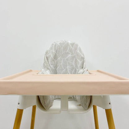 High chair with a light-coloured silicone tray cover and leaf patterned cushion cover on a plain background