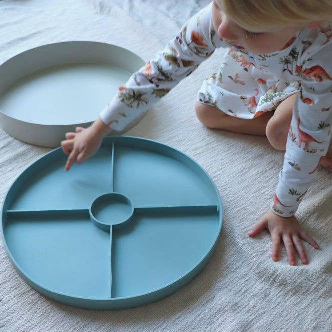 Child playing with a teal plate on a white floor