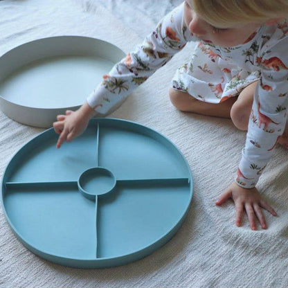 Child playing with a teal plate on a white floor