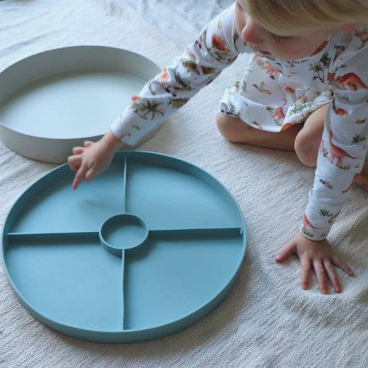 Child playing with a teal plate on a white floor