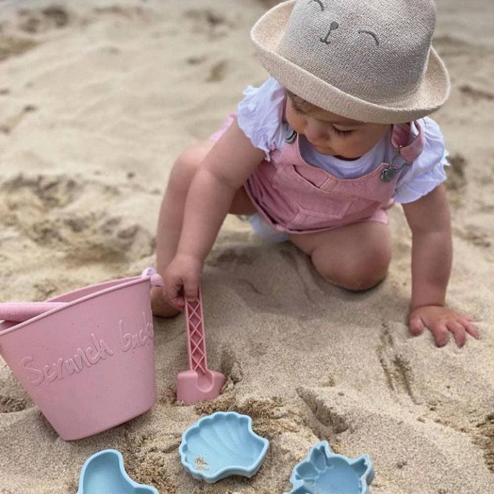Child playing in the sand with beach toys on a sandy beach.