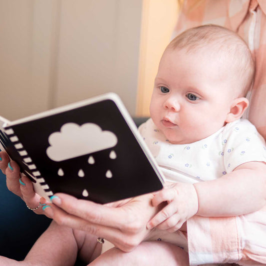 Baby being read to with a book featuring a cloud and raindrop illustration.