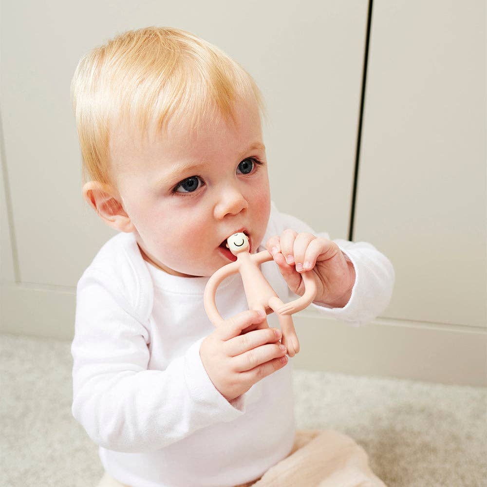Baby holding a pink teething ring against a neutral background