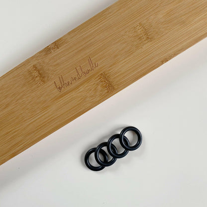 Four black rubber stoppers on a white surface with a wooden footrest in the background.