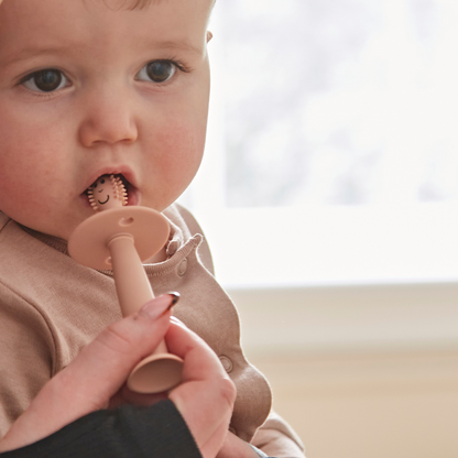 Baby using a pink silicone teether with a smiley face design.