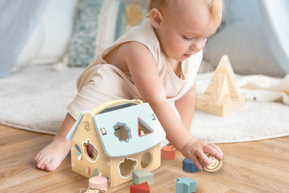 Baby playing with a shape sorter toy on a wooden floor.