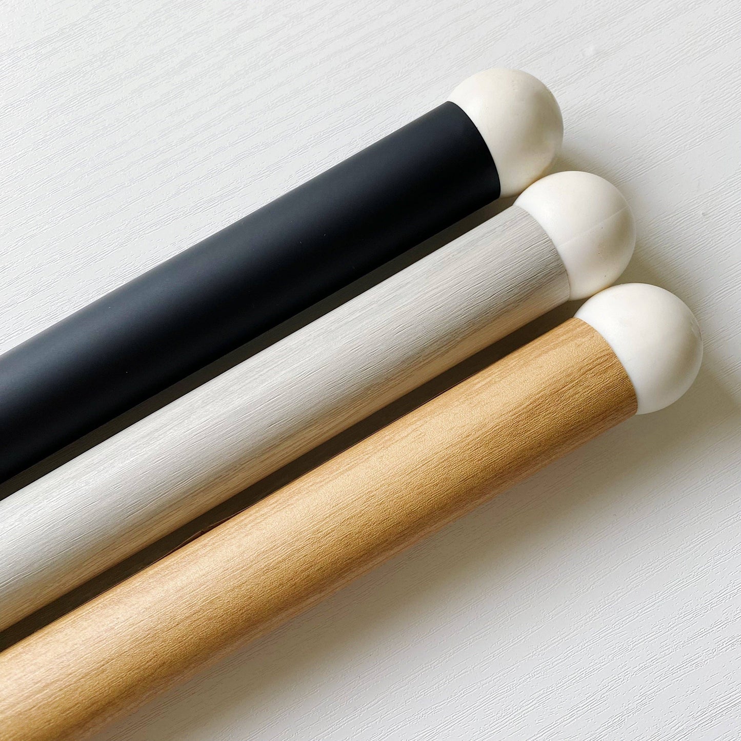 Three IKEA highchair legs with leg wrap in black, white, and natural wood on a light grey background