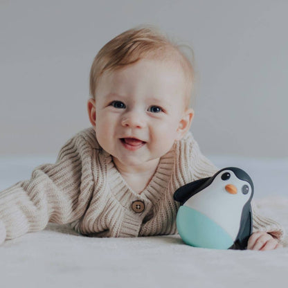 Baby holding a penguin toy on a plain background