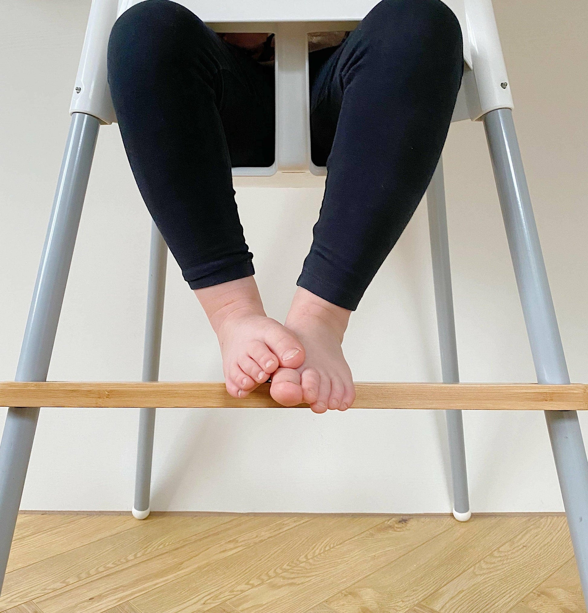 Person sitting on a high chair with legs crossed, feet resting on a wooden bar.